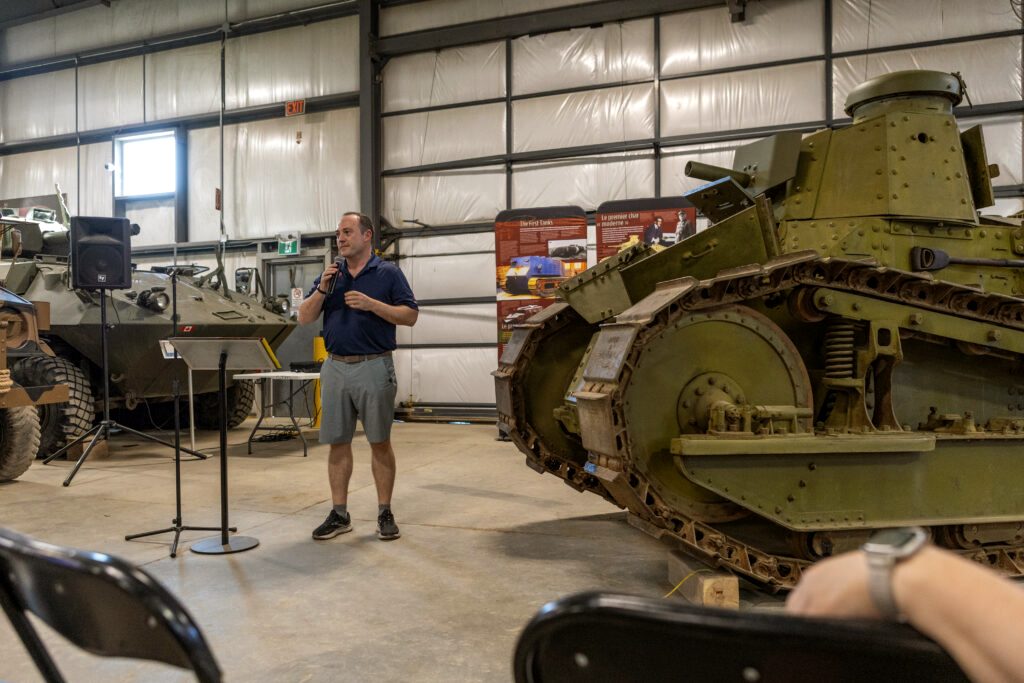 The museum's Renault M1917 light tank standing on the hall floor with a speaker addressing visitors beside it.